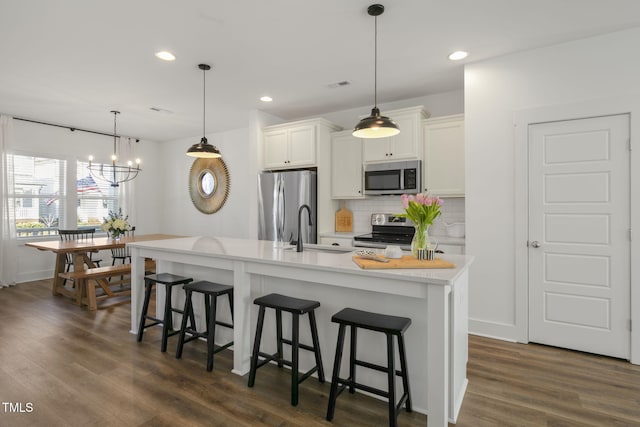 kitchen with a breakfast bar, a sink, appliances with stainless steel finishes, decorative backsplash, and dark wood-style floors