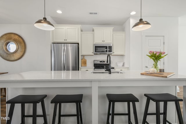 kitchen featuring stainless steel appliances, a sink, white cabinetry, hanging light fixtures, and decorative backsplash