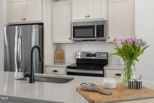 kitchen featuring light stone counters, appliances with stainless steel finishes, a sink, white cabinetry, and backsplash