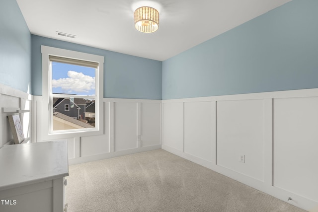 unfurnished room featuring a notable chandelier, light carpet, a wainscoted wall, a decorative wall, and visible vents