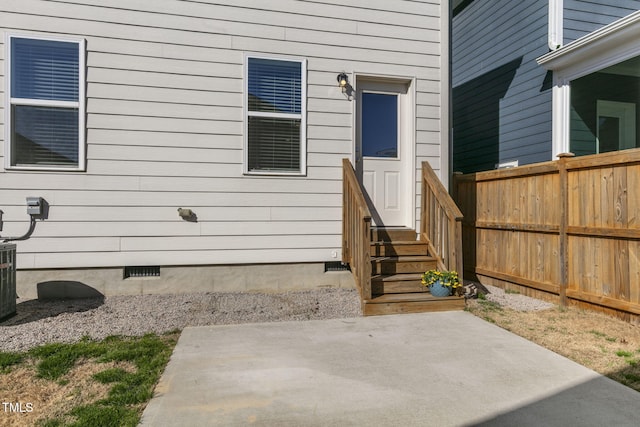 view of exterior entry featuring crawl space, fence, and a patio