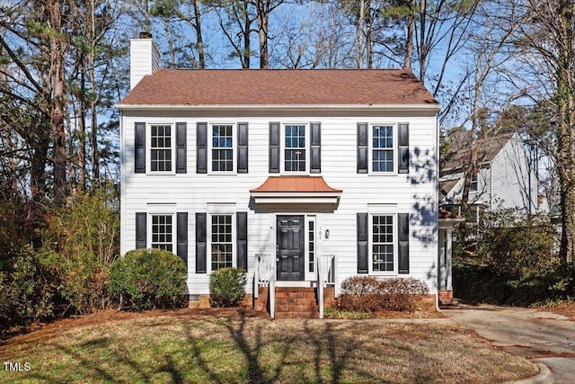 colonial home featuring a front yard, a chimney, and entry steps