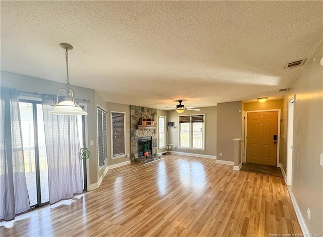 unfurnished living room with light wood-style flooring, a fireplace, visible vents, and a textured ceiling