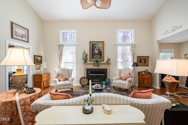 living room with a fireplace with flush hearth, wood finished floors, baseboards, and ceiling fan