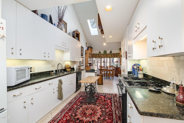 kitchen with lofted ceiling with skylight, light tile patterned floors, white appliances, white cabinetry, and a sink