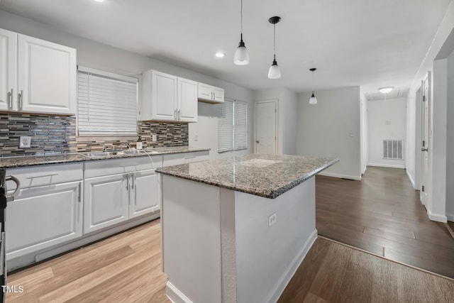 kitchen with tasteful backsplash, visible vents, light wood-style flooring, white cabinets, and dark stone counters