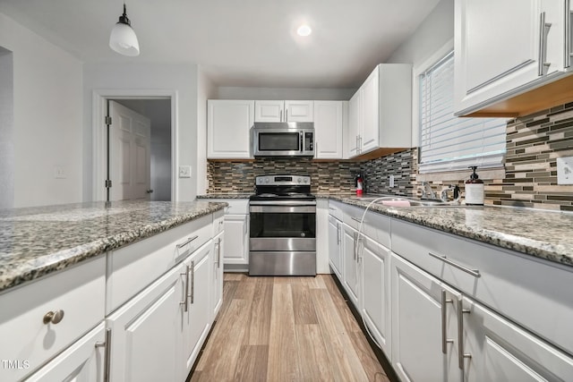 kitchen featuring appliances with stainless steel finishes, white cabinetry, light wood-style floors, and decorative backsplash