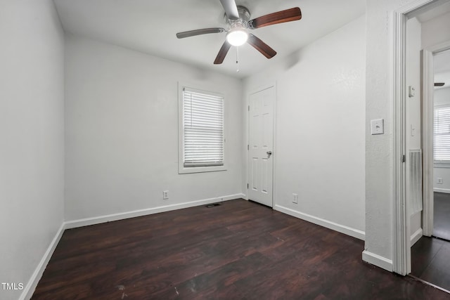 unfurnished bedroom featuring multiple windows, dark wood finished floors, and baseboards