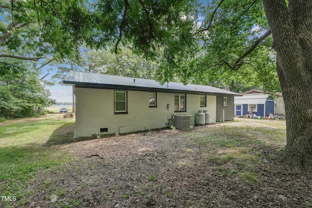 back of house featuring crawl space, brick siding, metal roof, and central AC