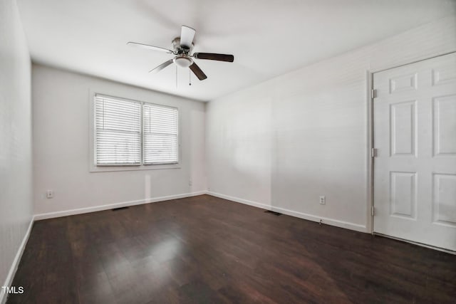 spare room featuring dark wood-style floors, visible vents, a ceiling fan, and baseboards