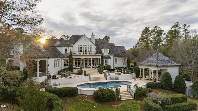 back of house with a fire pit, stucco siding, a chimney, a balcony, and an outdoor pool