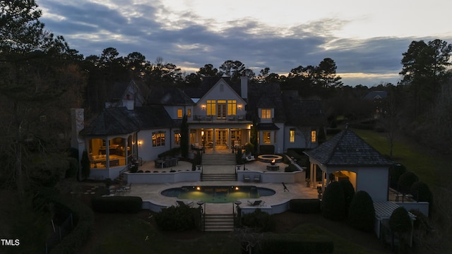 back of house featuring a balcony, an outdoor fire pit, a sunroom, a chimney, and a patio area