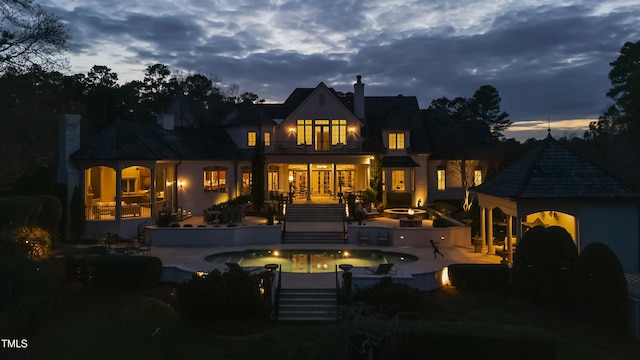 back of house at dusk featuring an outdoor pool, a balcony, a chimney, and a patio area