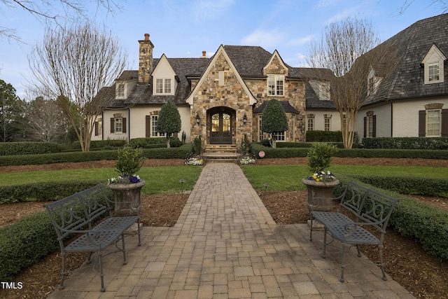 view of front of home featuring stone siding, french doors, a chimney, and a front lawn