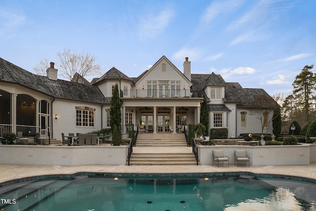 back of house featuring a patio, a balcony, an outdoor pool, and a chimney