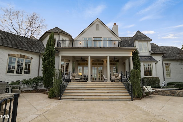 back of house with brick siding, french doors, a balcony, ceiling fan, and a chimney