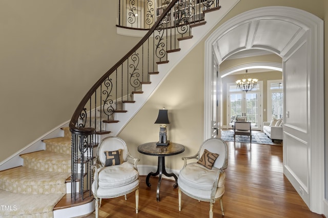 staircase featuring arched walkways, a chandelier, baseboards, and wood finished floors