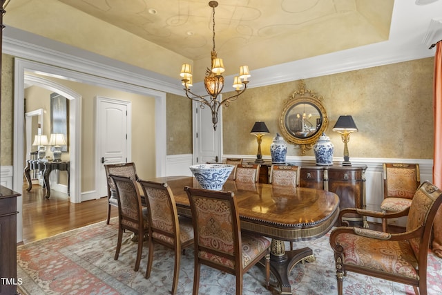 dining area with a wainscoted wall, an inviting chandelier, a tray ceiling, and wood finished floors