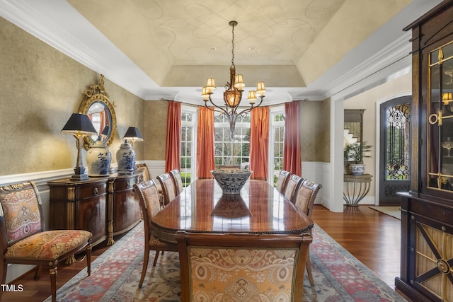 dining room featuring a raised ceiling, an inviting chandelier, wood finished floors, and wainscoting