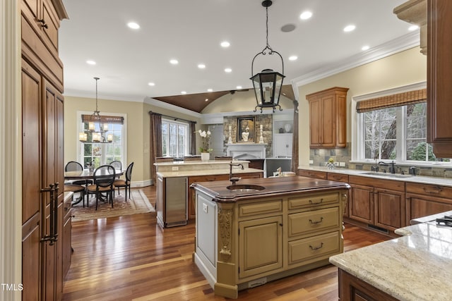 kitchen featuring ornamental molding, a kitchen island with sink, dark wood-style flooring, and a sink