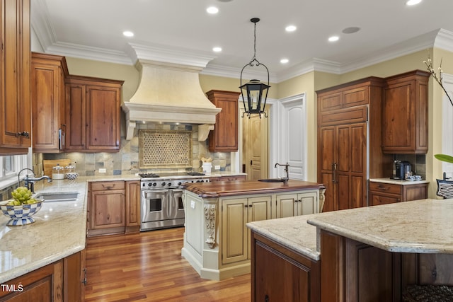 kitchen with wood finished floors, a kitchen island, custom exhaust hood, range with two ovens, and a sink