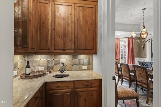 kitchen with pendant lighting, a sink, tasteful backsplash, glass insert cabinets, and light stone countertops