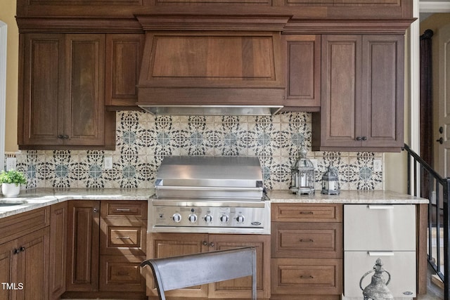 kitchen featuring ventilation hood, light stone countertops, refrigerator, decorative backsplash, and brown cabinets