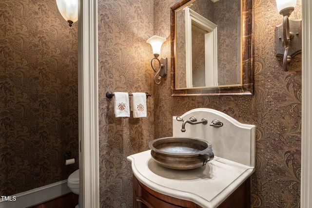 half bathroom featuring toilet, vanity, and wallpapered walls