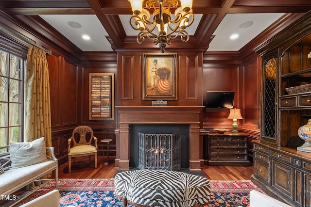 living area featuring a fireplace with flush hearth, coffered ceiling, crown molding, and wood finished floors