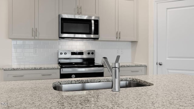 kitchen featuring stainless steel appliances, white cabinets, backsplash, and light stone counters