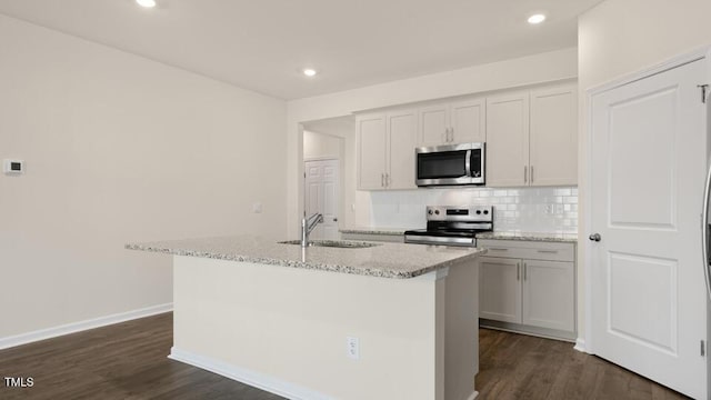 kitchen featuring tasteful backsplash, an island with sink, light stone counters, stainless steel appliances, and a sink