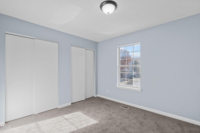 unfurnished bedroom featuring multiple closets, light colored carpet, visible vents, and baseboards