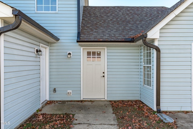 view of exterior entry with roof with shingles