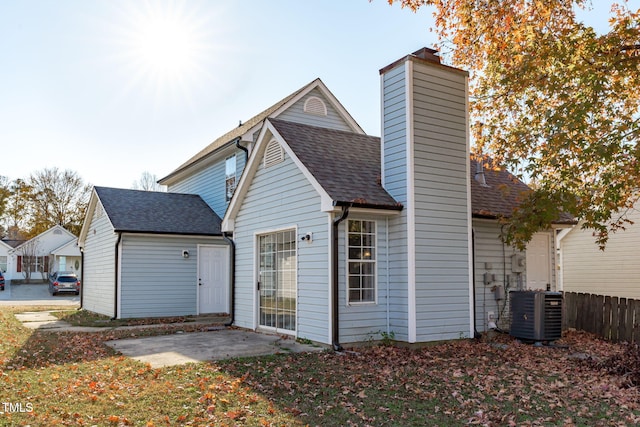 rear view of house with roof with shingles, a chimney, central AC unit, and a patio