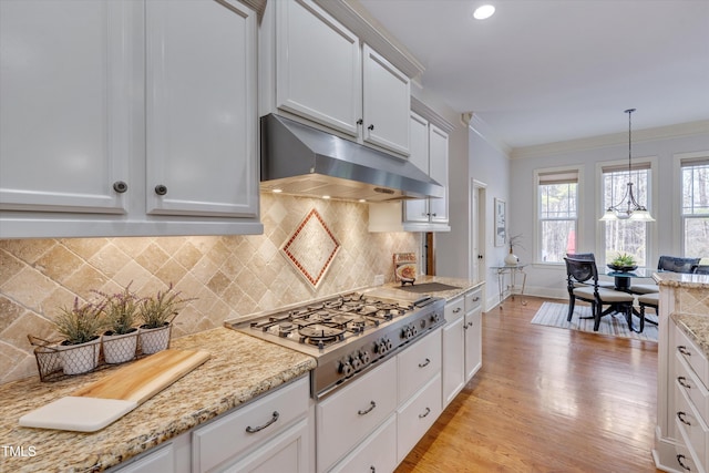 kitchen featuring under cabinet range hood, white cabinets, stainless steel gas stovetop, ornamental molding, and pendant lighting