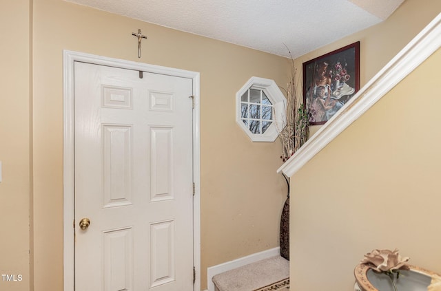 carpeted foyer with a textured ceiling and baseboards