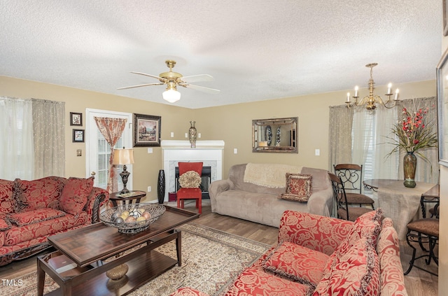 living room featuring a fireplace, ceiling fan with notable chandelier, wood finished floors, and a textured ceiling