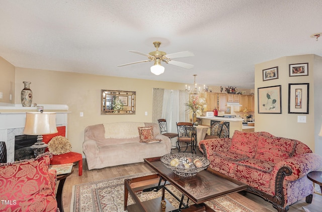 living area featuring a textured ceiling, wood finished floors, a fireplace, and ceiling fan with notable chandelier