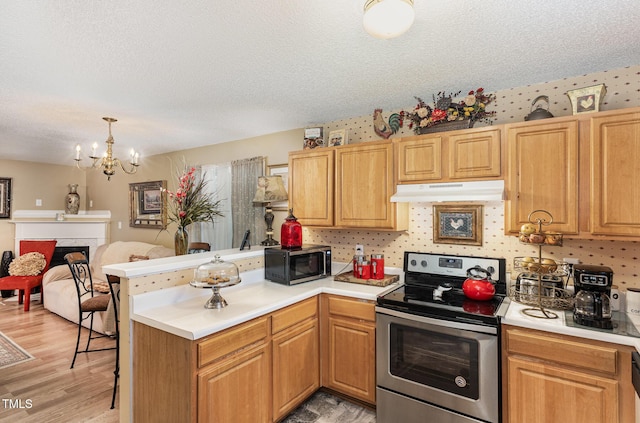 kitchen with under cabinet range hood, appliances with stainless steel finishes, a peninsula, a fireplace, and light countertops