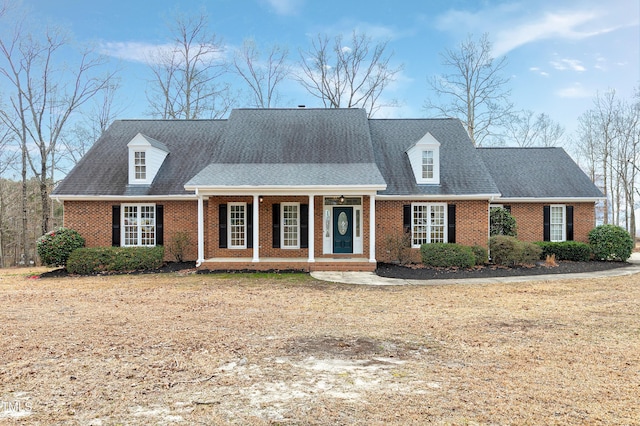 cape cod home with brick siding, roof with shingles, and a porch