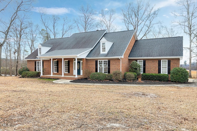 cape cod house featuring covered porch, roof with shingles, and brick siding