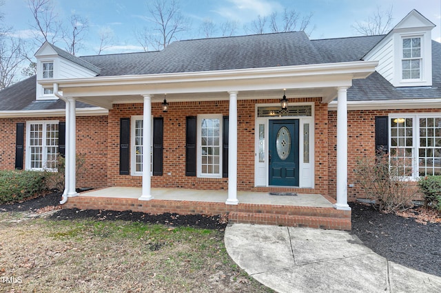 property entrance featuring covered porch, brick siding, and a shingled roof