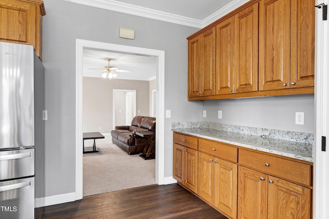 kitchen with brown cabinetry, freestanding refrigerator, crown molding, and light stone counters