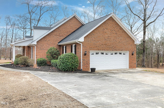 view of side of property with a garage, driveway, brick siding, and roof with shingles