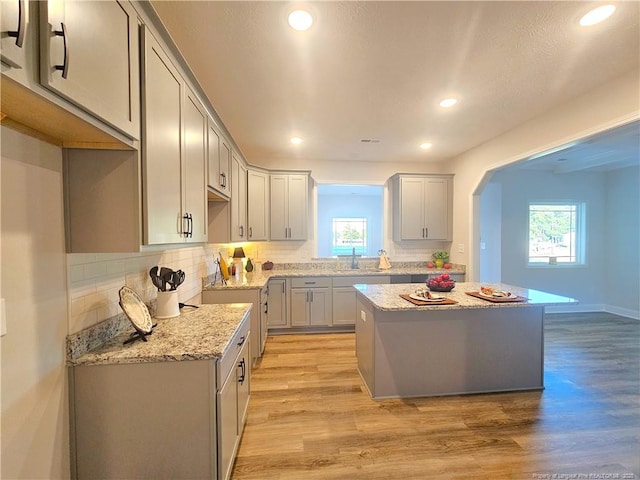 kitchen with light stone counters, a kitchen island, gray cabinetry, and light hardwood / wood-style floors