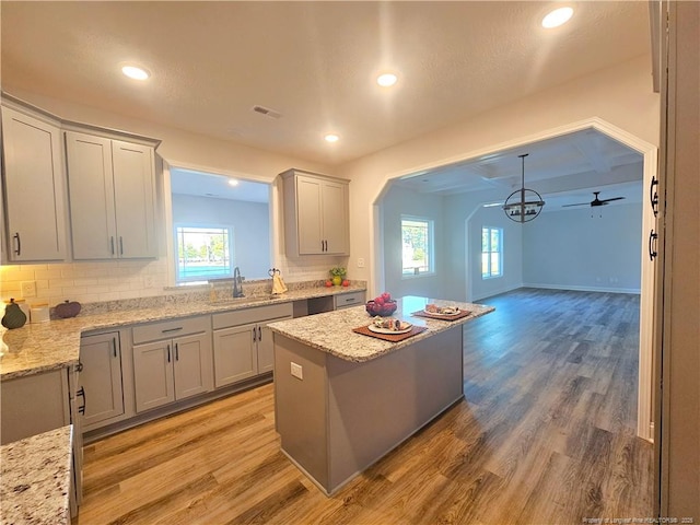 kitchen with gray cabinets, a kitchen island, sink, and light stone counters