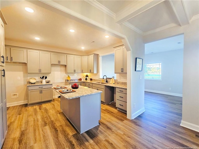 kitchen with a center island, light stone countertops, light hardwood / wood-style floors, sink, and decorative backsplash