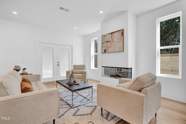 living room with recessed lighting, a multi sided fireplace, visible vents, french doors, and light wood finished floors