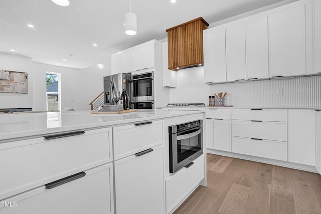 kitchen with light wood finished floors, white cabinets, appliances with stainless steel finishes, decorative light fixtures, and light countertops