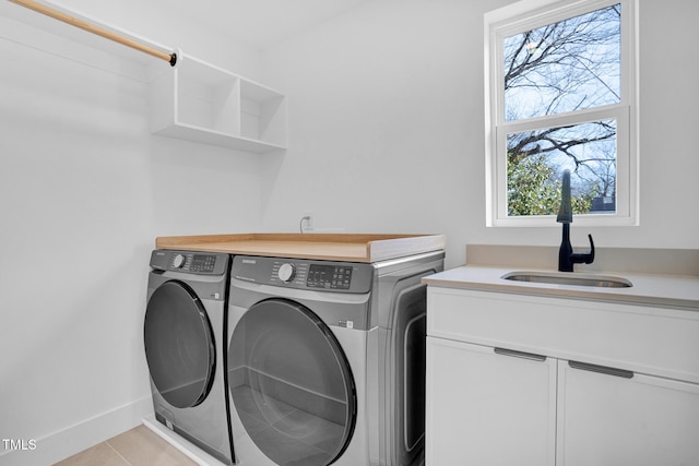 clothes washing area with washer and clothes dryer, light tile patterned floors, cabinet space, a sink, and baseboards